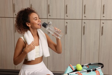 Beautiful young African American woman drinking water in locker room