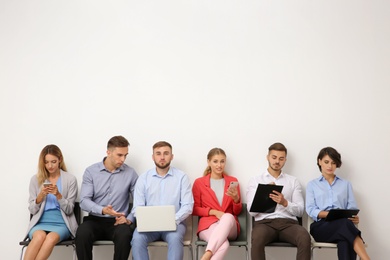 Group of young people waiting for job interview near light wall