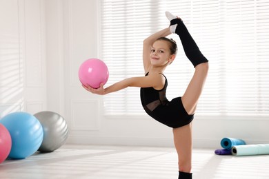 Cute little gymnast with ball doing standing split indoors