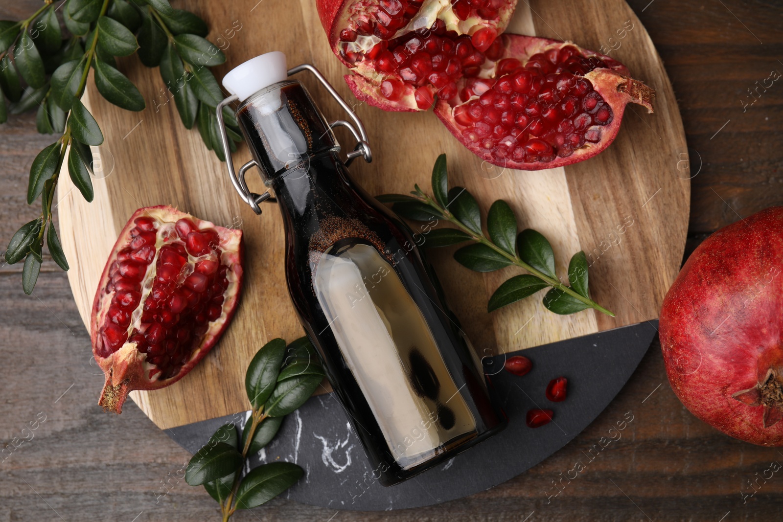 Photo of Tasty pomegranate sauce in bottle, fruits and branches on wooden table, flat lay