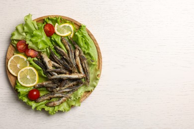 Photo of Tray with delicious fried anchovies, lemon slices, cherry tomatoes and lettuce leaves on white wooden table, top view. Space for text