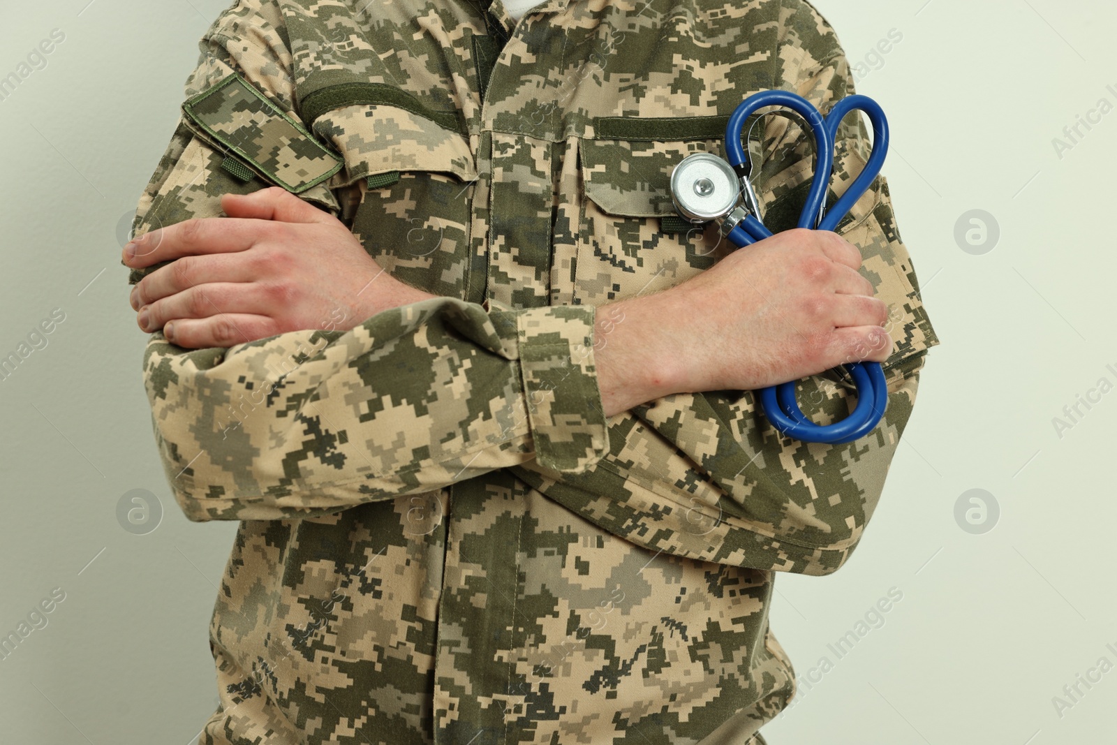 Photo of Man in military uniform with crossed arms and stethoscope on light background, closeup. Health care concept