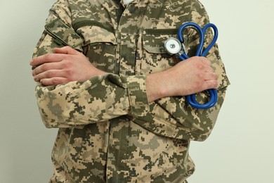 Man in military uniform with crossed arms and stethoscope on light background, closeup. Health care concept