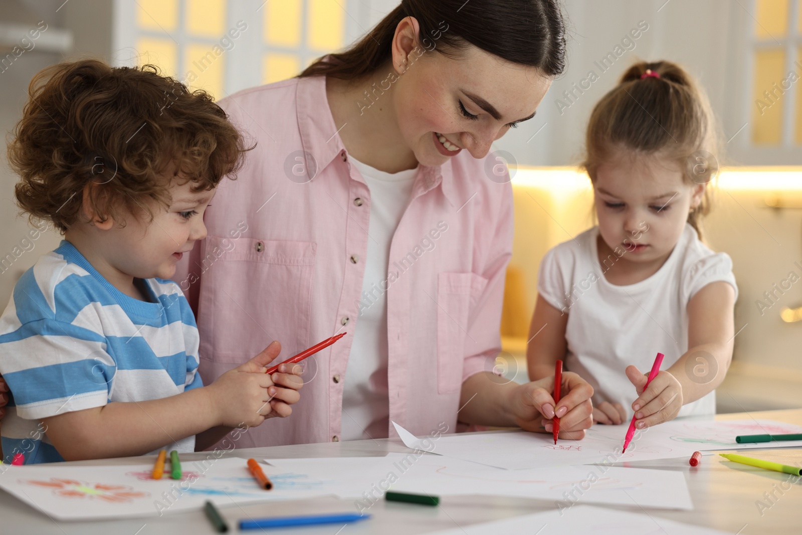 Photo of Mother and her little children drawing with colorful markers at table in kitchen