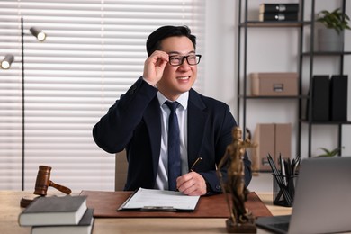 Happy notary writing notes at wooden table in office