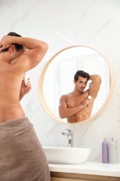 Handsome young man applying deodorant in bathroom