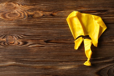 Photo of Popped yellow balloon on wooden background, top view with space for text