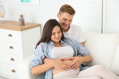 Young husband and his pregnant wife resting on sofa at home