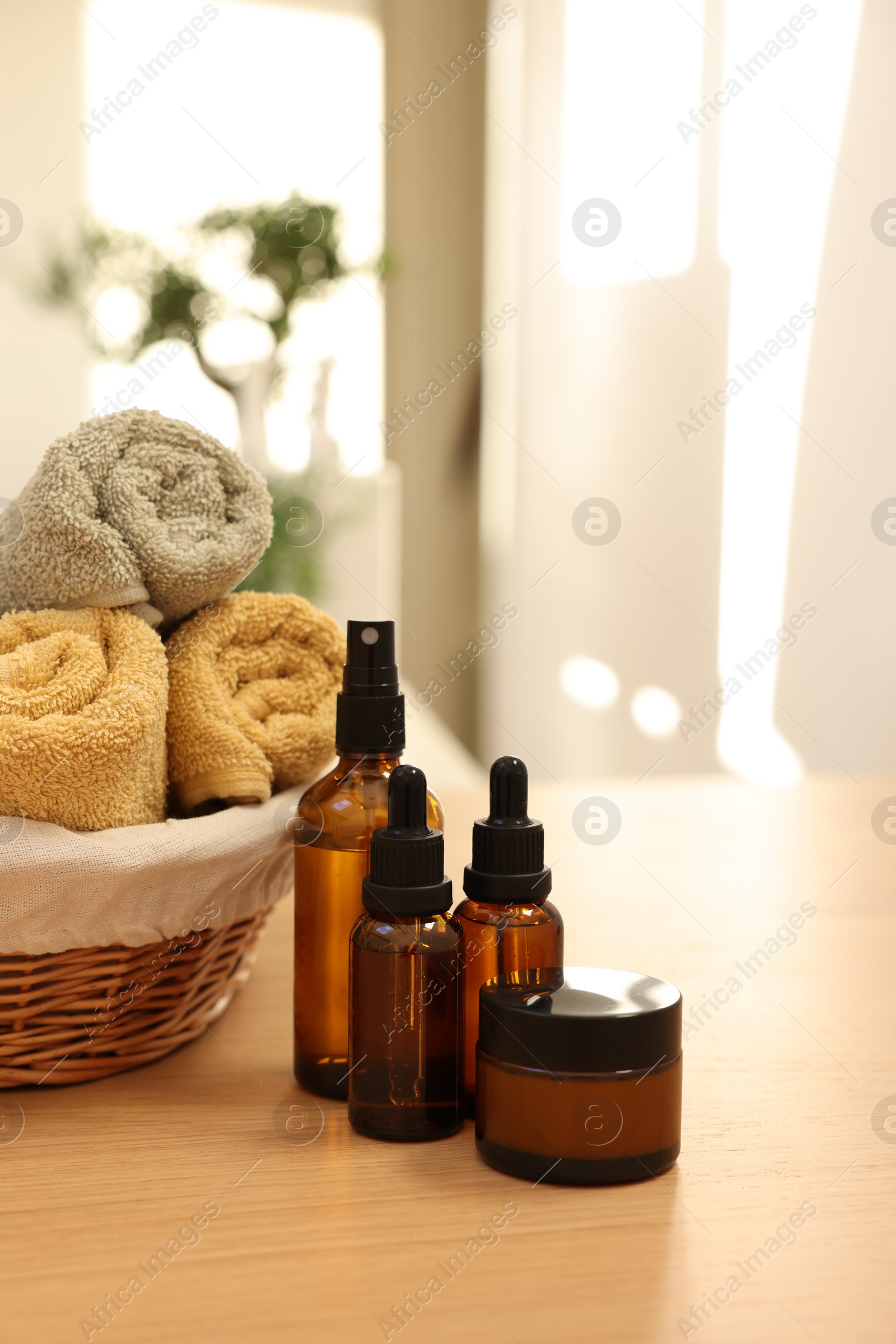 Photo of Bottles of essential oils, towels and jar with cream on wooden table indoors. Spa time