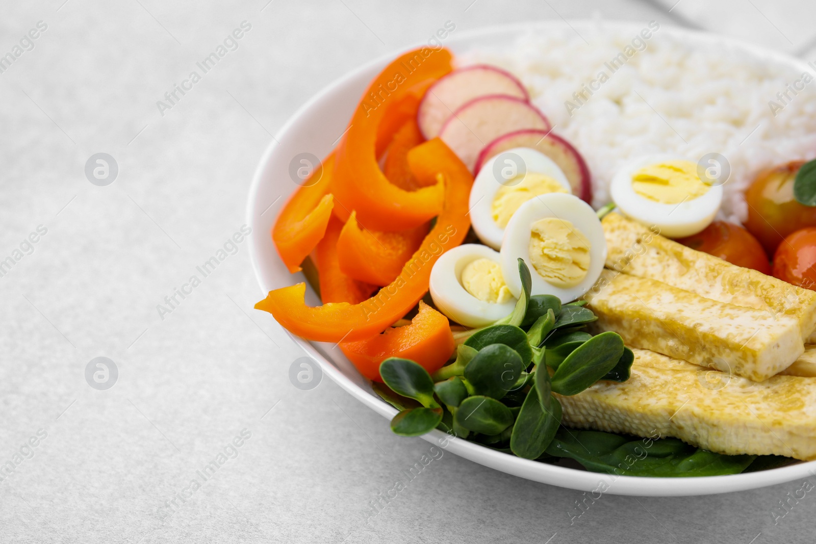 Photo of Delicious poke bowl with basil, vegetables, eggs and tofu on light grey table, closeup. Space for text