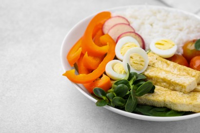 Delicious poke bowl with basil, vegetables, eggs and tofu on light grey table, closeup. Space for text