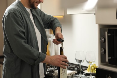 Smiling man opening wine bottle with corkscrew at countertop indoors, closeup