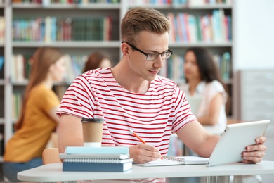 Photo of Young man working on tablet at table in library