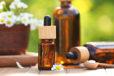 Photo of Bottles of chamomile essential oil and flowers on wooden table, closeup