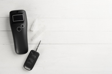 Photo of Modern breathalyzer, mouthpieces and car key on white wooden background, flat lay. Space for text