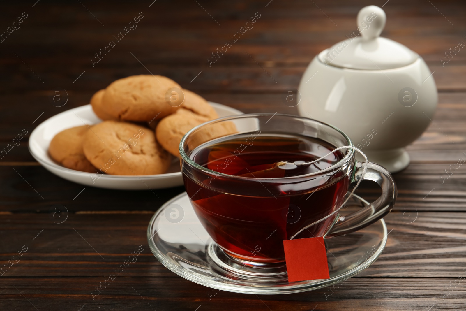 Photo of Tea bag in glass cup of hot water and cookies on wooden table