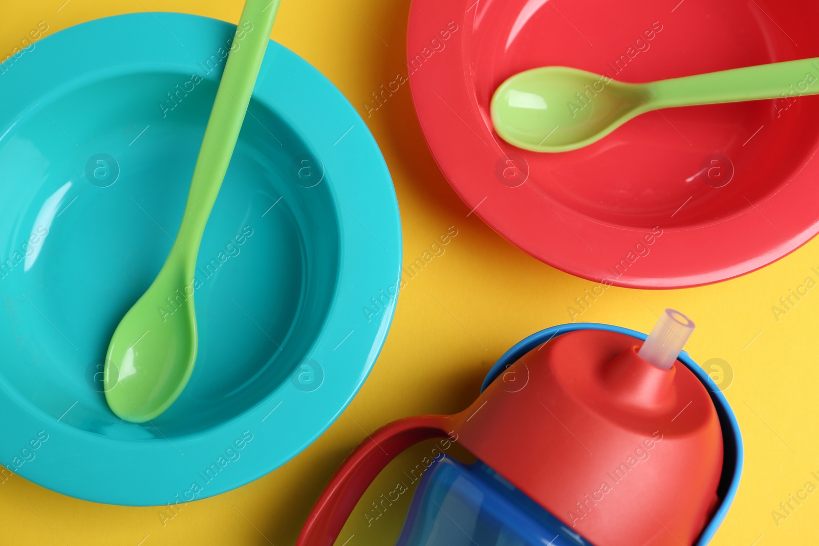 Photo of Set of colorful plastic dishware on yellow background, flat lay. Serving baby food