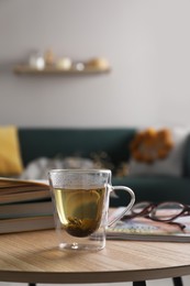 Glass cup of freshly brewed tea on wooden table in living room. Cozy home atmosphere