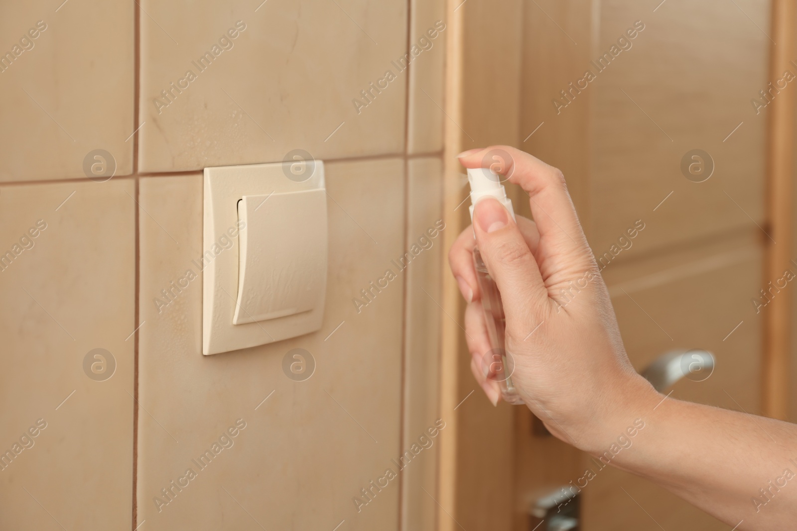 Photo of Woman spraying antiseptic onto light switch indoors, closeup