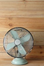 Photo of Electric fan on table near wooden wall. Summer heat