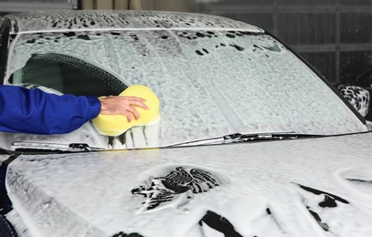 Photo of Worker cleaning automobile windshield with sponge at professional car wash, closeup