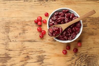 Tasty dried cranberries in bowl and fresh ones on wooden table, top view. Space for text