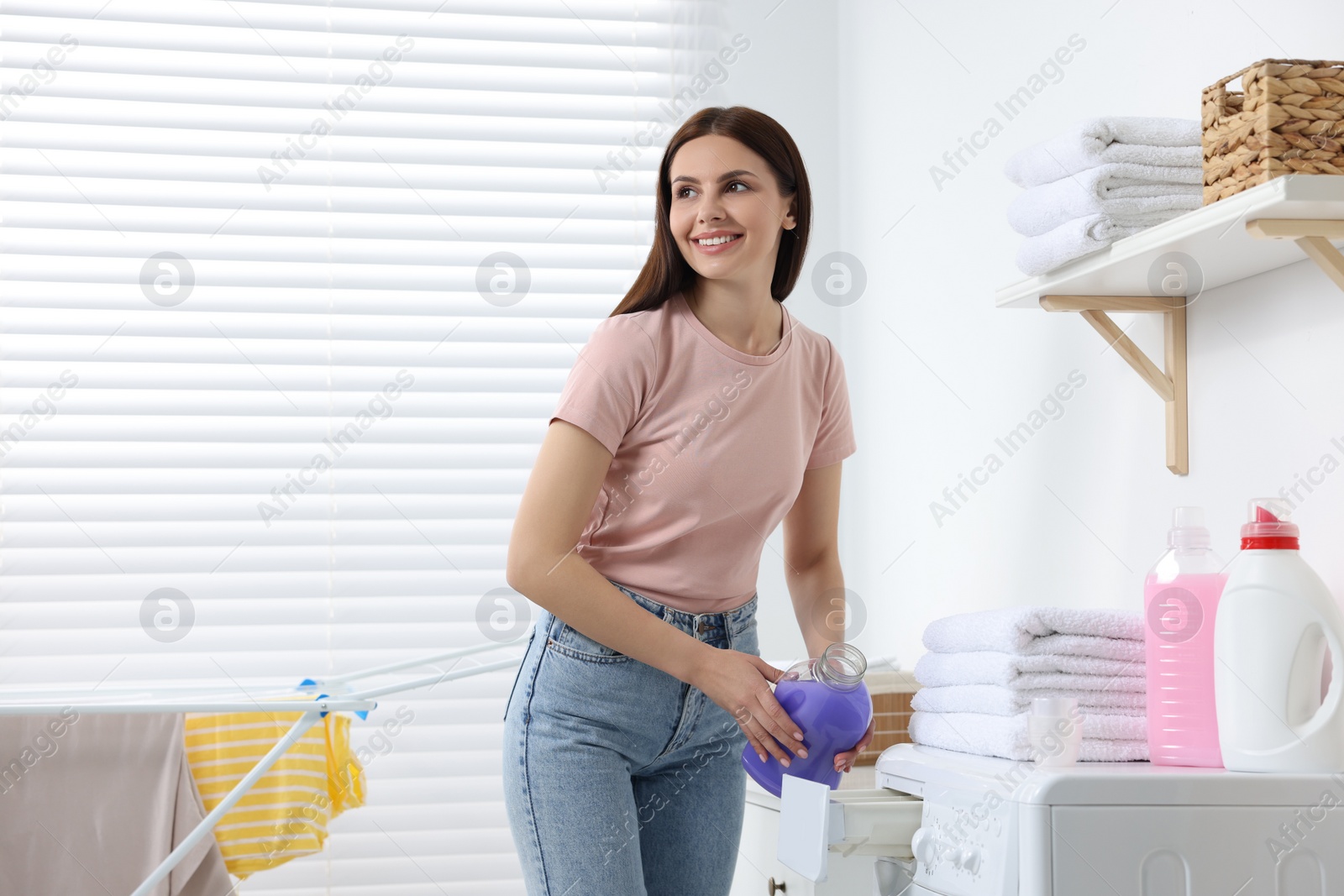 Photo of Woman pouring fabric softener into washing machine in bathroom