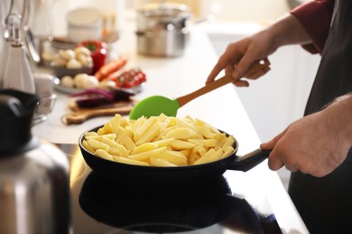 Photo of Man stirring cut raw potatoes in frying pan, closeup