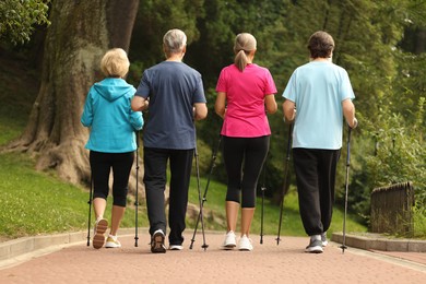 Photo of Group of senior people performing Nordic walking outdoors, back view