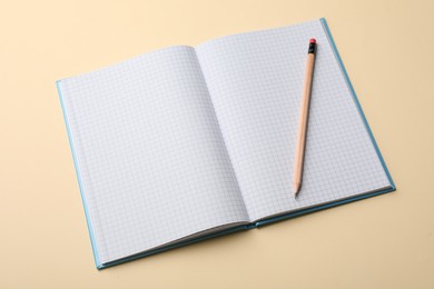 Photo of Open notebook with blank sheets and pencil on beige background