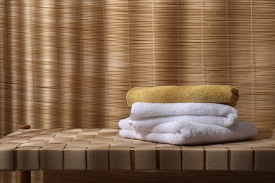 Photo of Stacked soft towels on wicker bench indoors, space for text