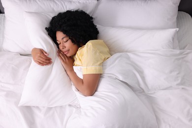 Photo of Beautiful young woman sleeping in soft bed, top view