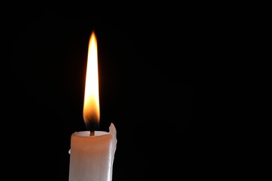 Photo of Burning candle on black background, closeup. Space for text
