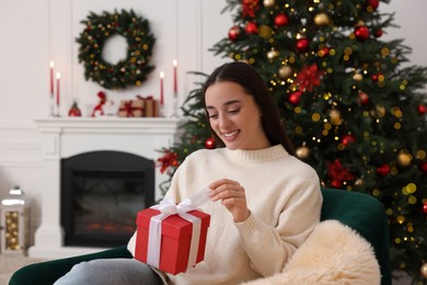 Happy young woman opening Christmas gift at home