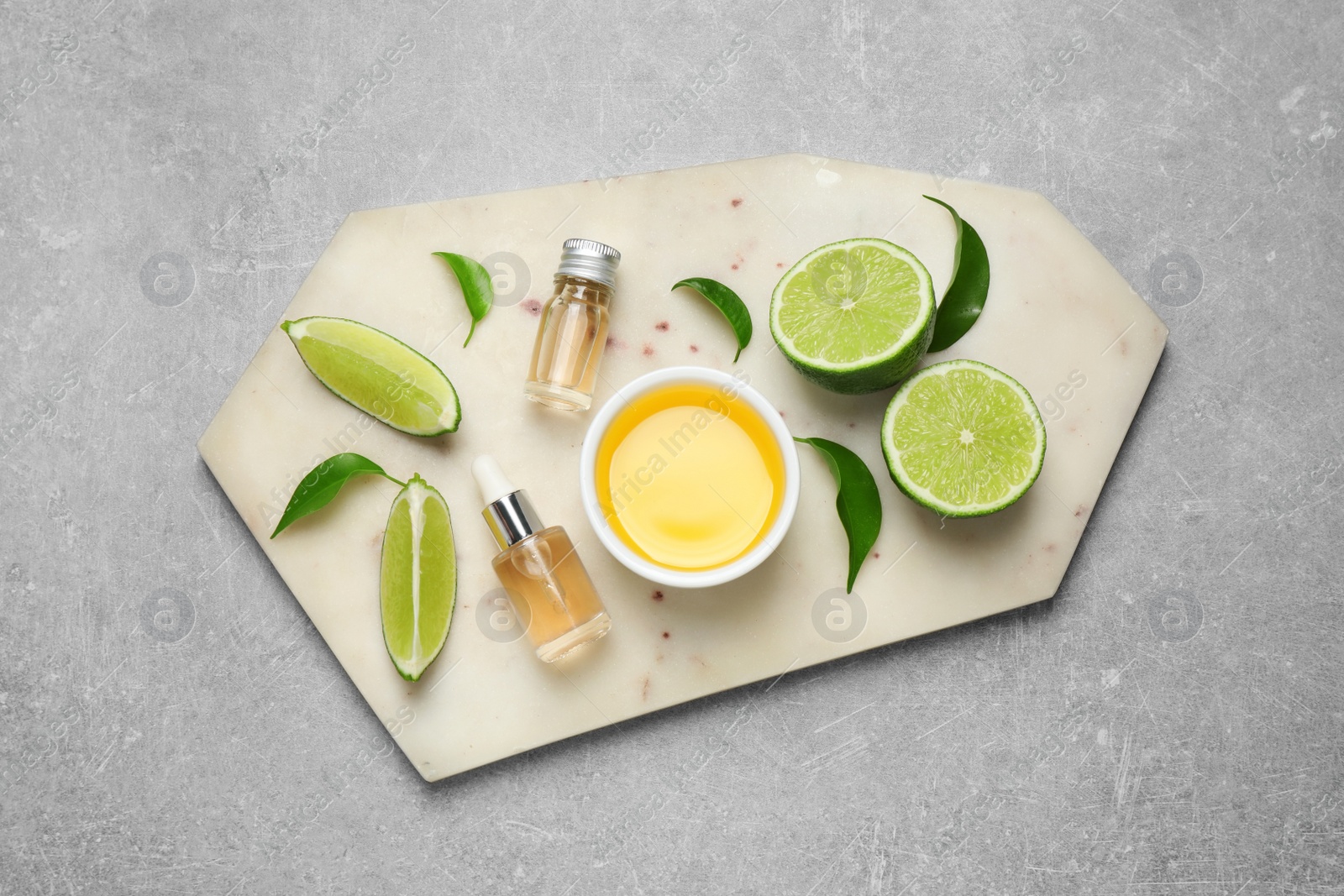 Photo of Lime essential oil and cut citrus fruits on light grey table, top view