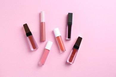 Photo of Different lip glosses on pink background, flat lay