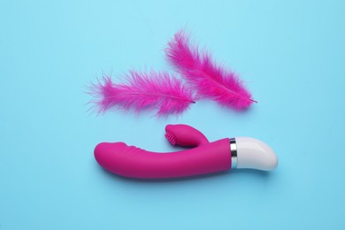 Pink vaginal vibrator and feathers on light blue background, flat lay. Sex toy