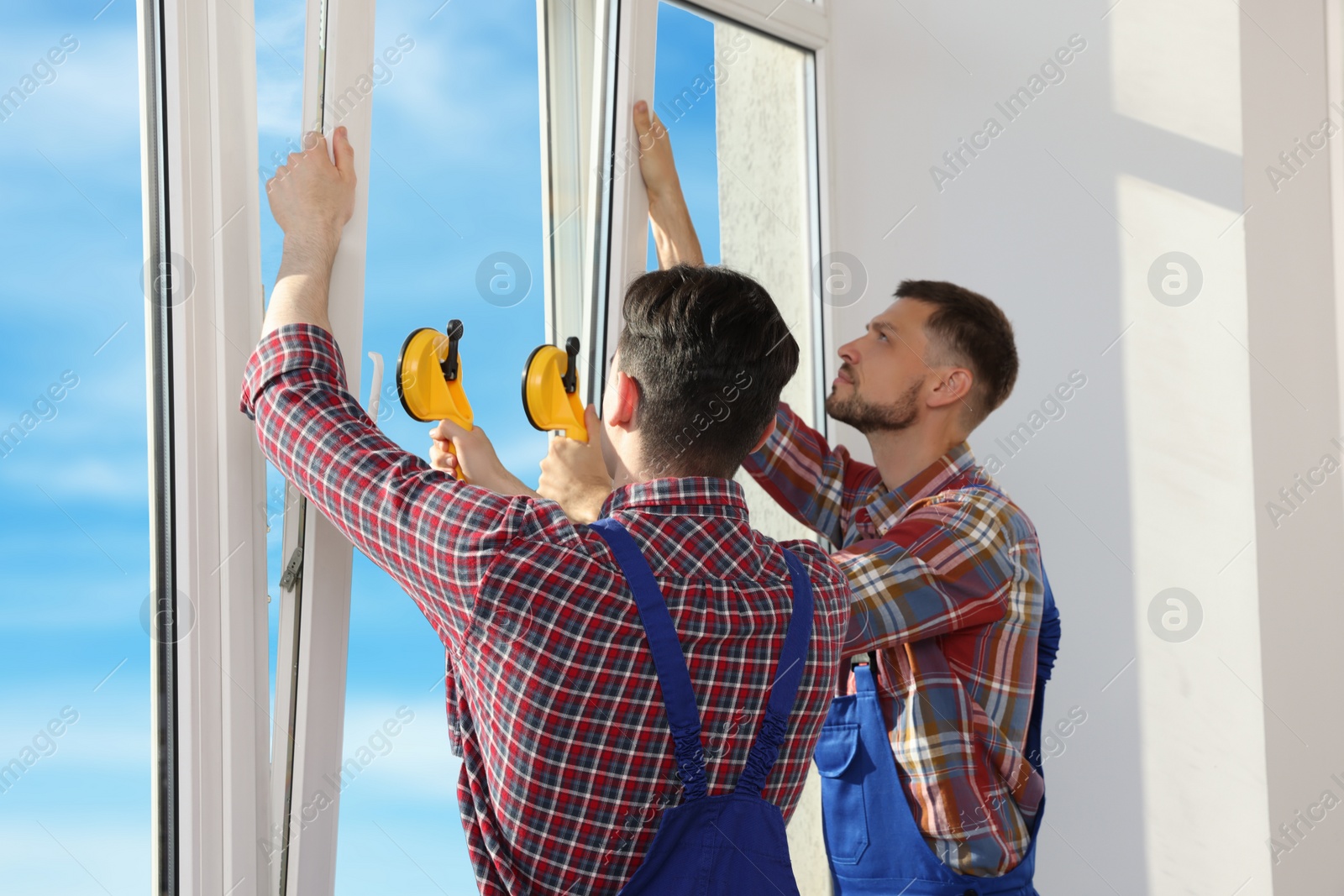 Photo of Workers using suction lifters during plastic window installation indoors