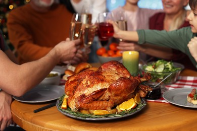 Photo of Family clinking glasses of drinks at festive dinner, focus on delicious baked turkey. Christmas celebration