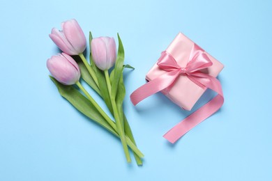 Photo of Beautiful gift box with bow and tulips on light blue background, flat lay