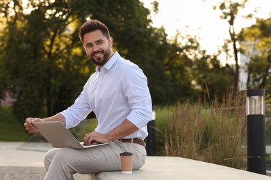 Photo of Handsome young man using laptop on stone bench outdoors. Space for text