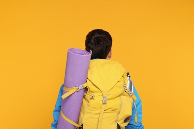 Photo of Man with backpack and mat on orange background, back view. Active tourism