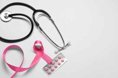 Photo of Breast cancer awareness. Pink ribbon, stethoscope and pills on white background, flat lay. Space for text