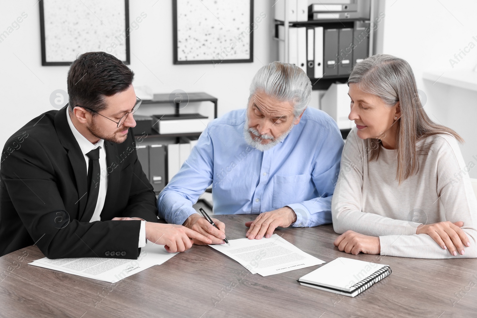 Photo of Elderly couple consulting insurance agent about pension plan at wooden table indoors