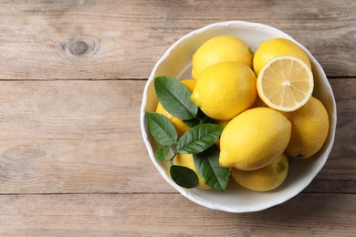 Fresh lemons and green leaves on wooden table, top view. Space for text