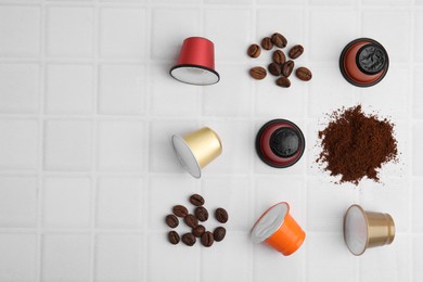 Photo of Many coffee capsules, powder and beans on white tiled table, flat lay. Space for text