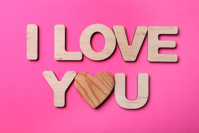 Photo of Phrase I Love You made of wooden heart and letters on pink background, above view