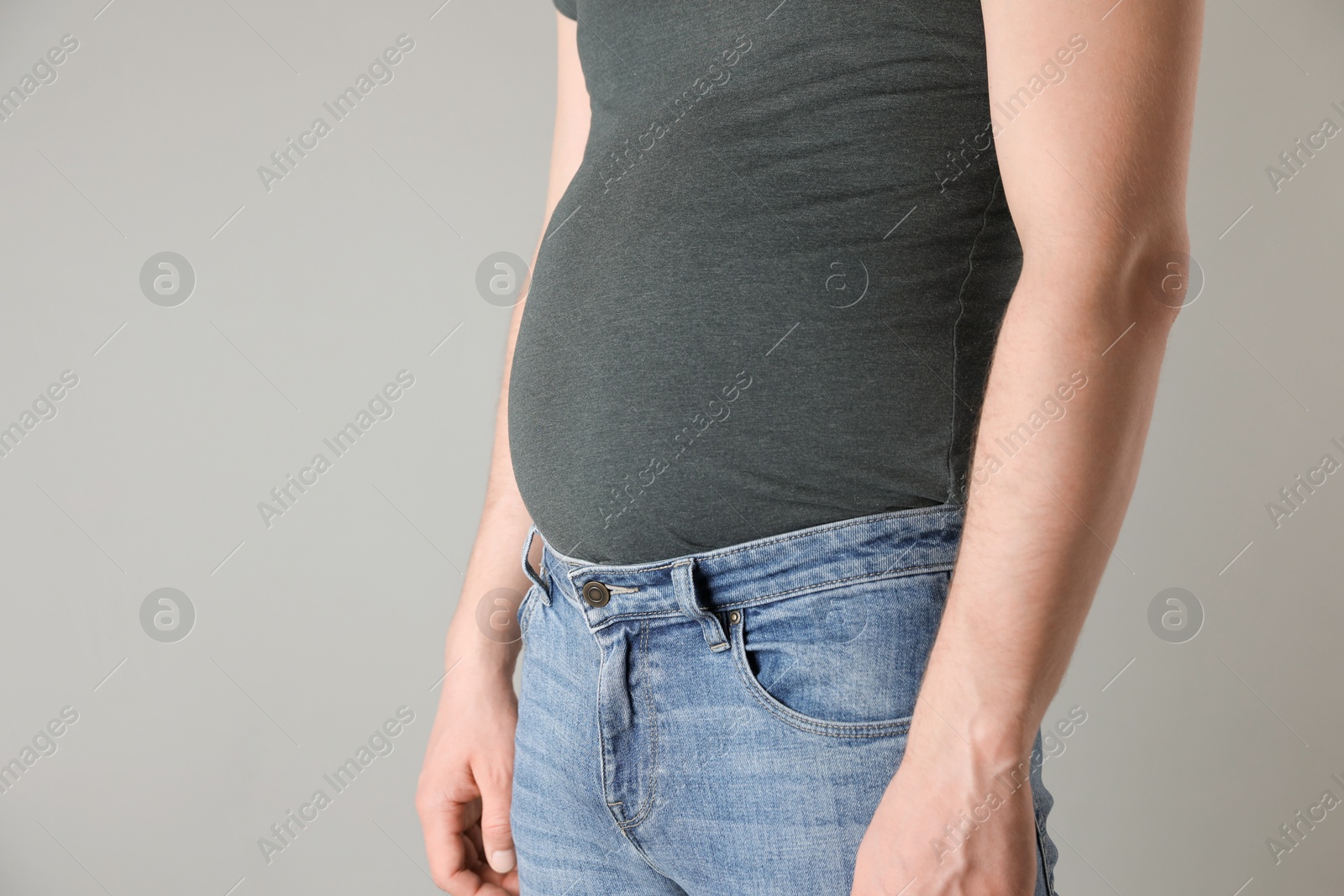 Photo of Overweight man in tight tshirt and jeans on light grey background, closeup. Space for text