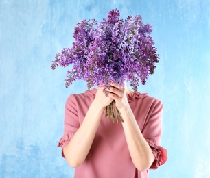 Photo of Woman closing face with bouquet of beautiful lilac flowers on color background