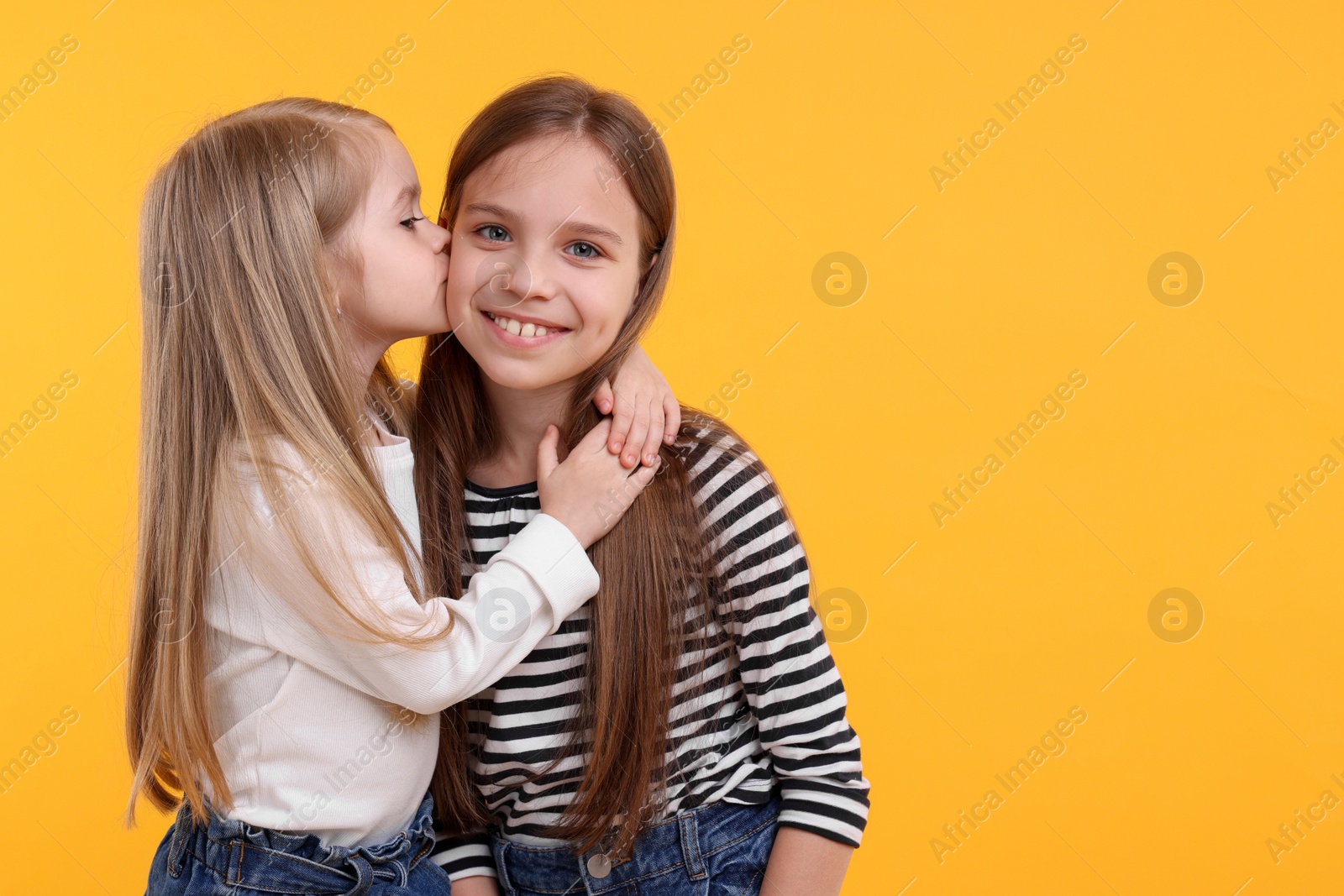 Photo of Portrait of cute little sisters on orange background, space for text